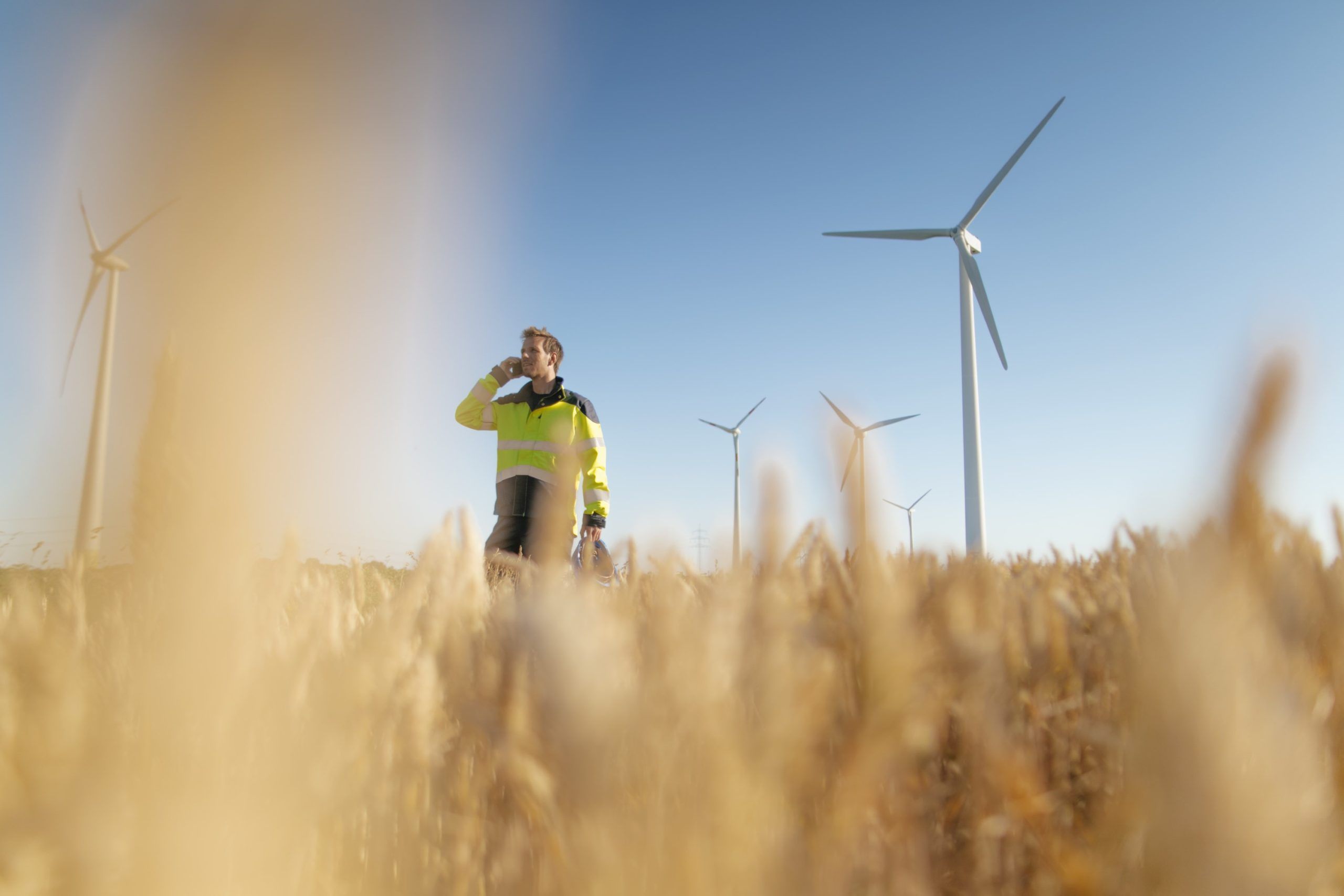 Engineer standing in a field at a wind farm talking on cell phone
